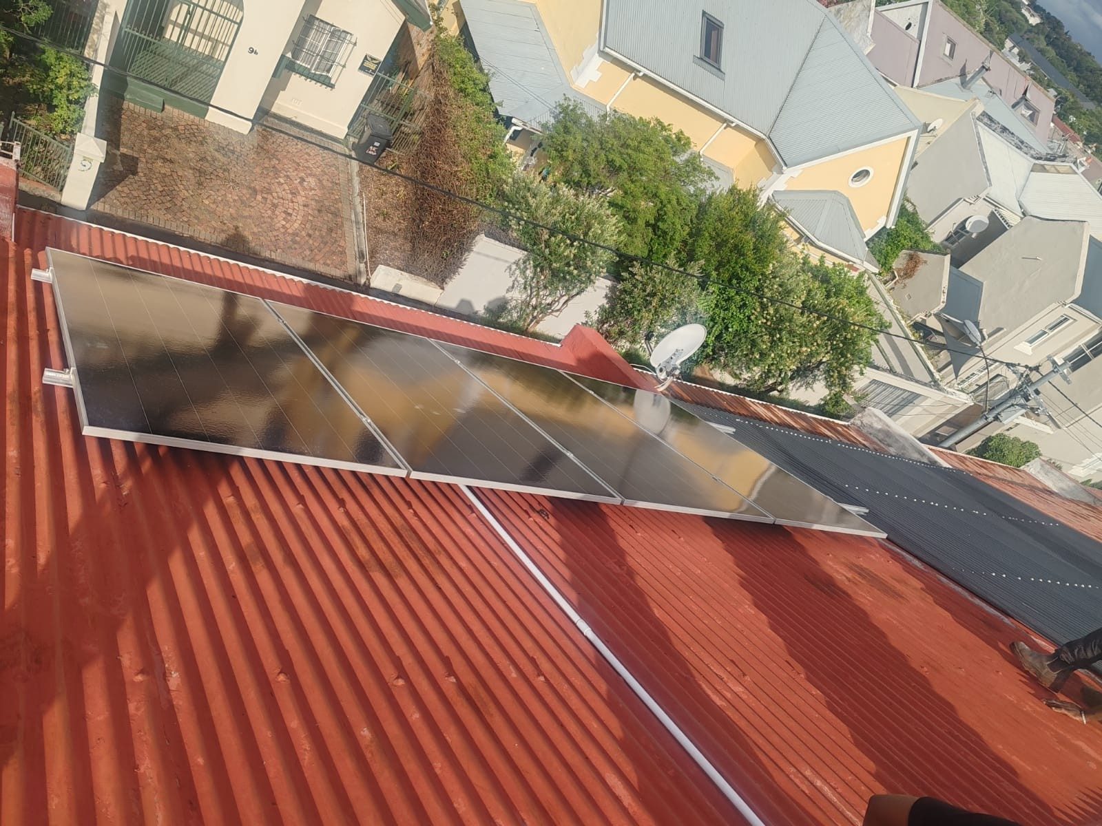 Solar panels mounted on a red corrugated iron roof overlooking Cape Town houses